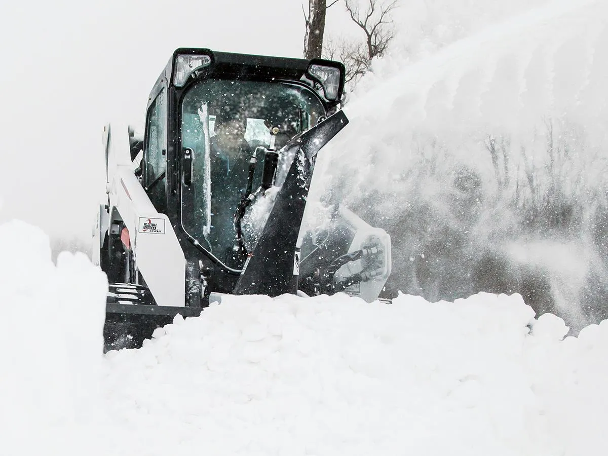A snow plow is blowing snow on the ground.