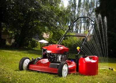 A red lawn mower sitting in the grass next to a gas can.